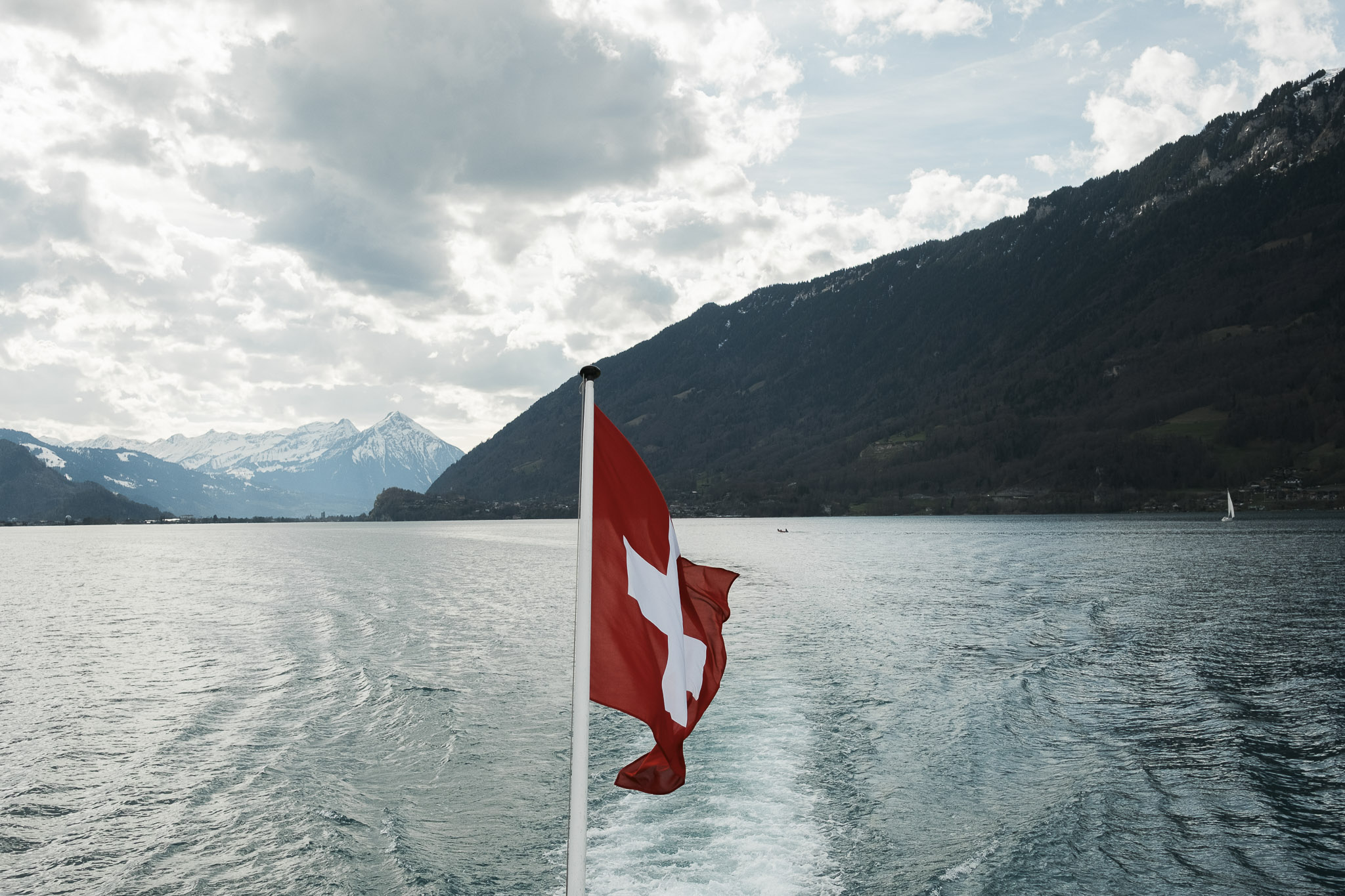 Swiss flag on a boat cruising Lake Brienz with alpine mountain scenery near Iseltwald.
