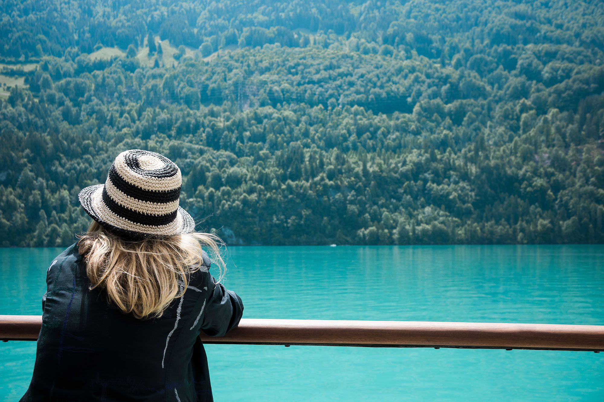 Woman wearing a sun hat enjoys the view of the turquoise-blue Lake Brienz during a boat cruise.